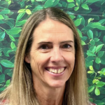 Smiling woman with long brown hair in front of a leafy green background.