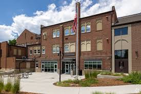Brick building with large windows, a flagpole, and landscaped area in front, under a partly cloudy sky.